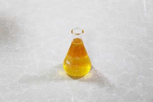 Dark amber heavy alkylbenzene oil in industrial drum, petrochemical facility background